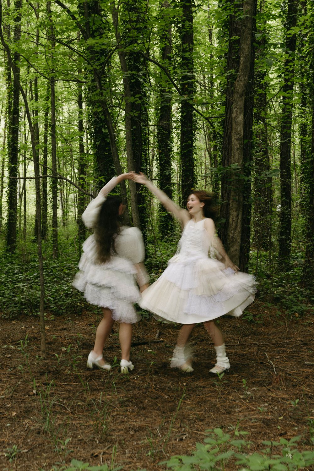 Two women twirling in white dresses in a forest showing motion blur, fairytale vibes