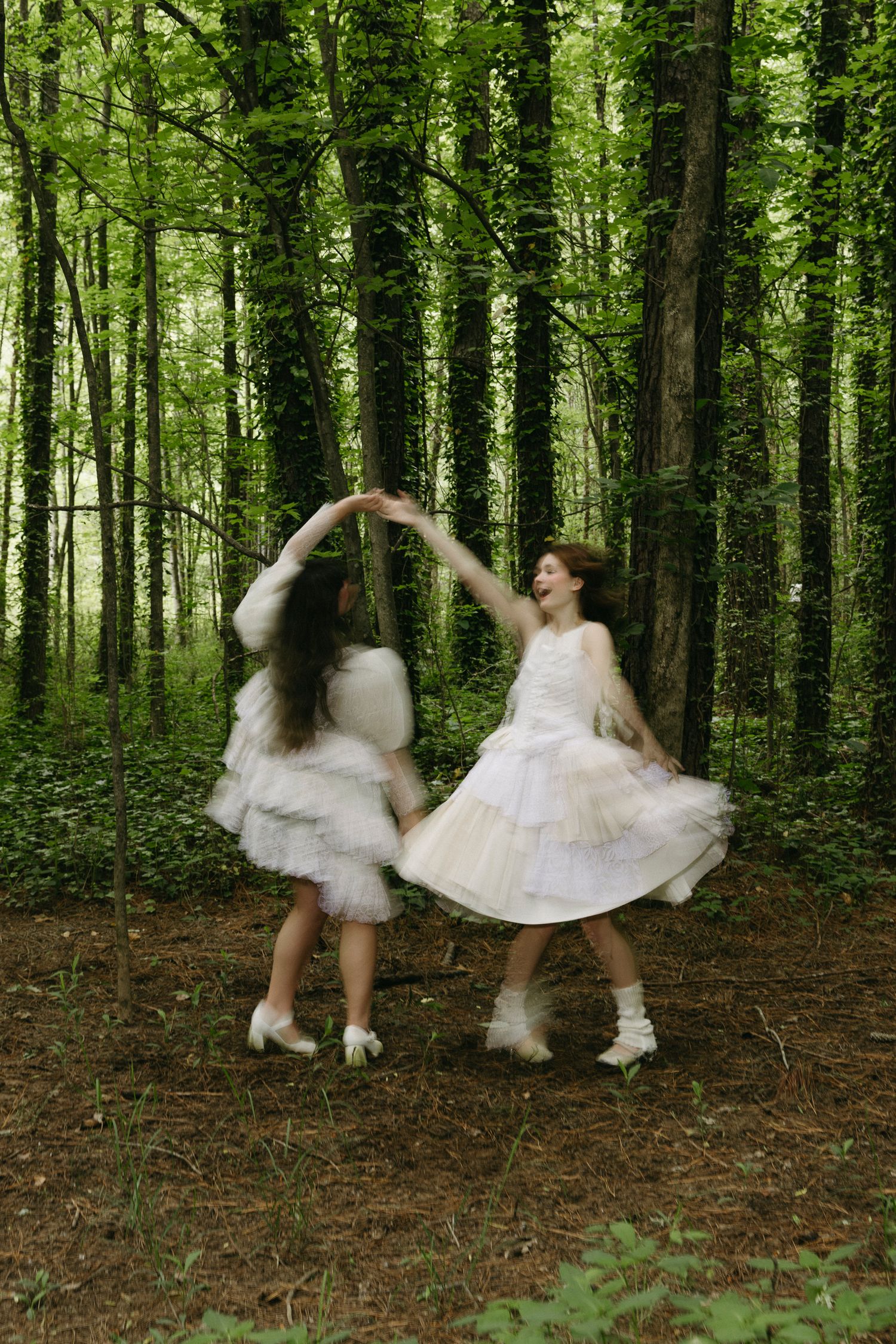 Two women twirling in white dresses in a forest showing motion blur, fairytale vibes