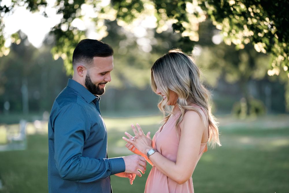 A couple shares an intimate moment in a sunny park as they look down at something together.