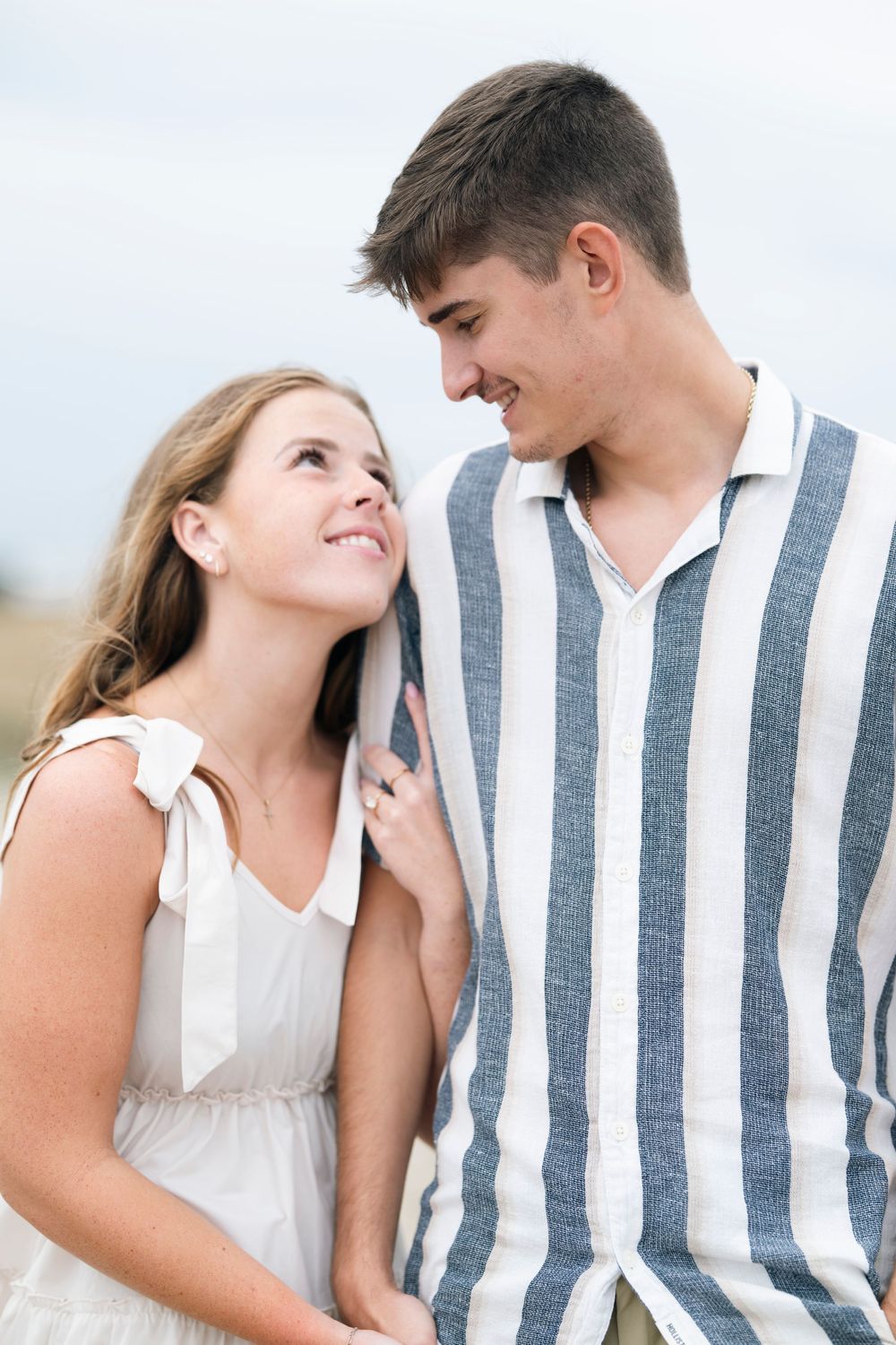 A couple in white and striped outfits share intimate moments in a romantic outdoor photo series.