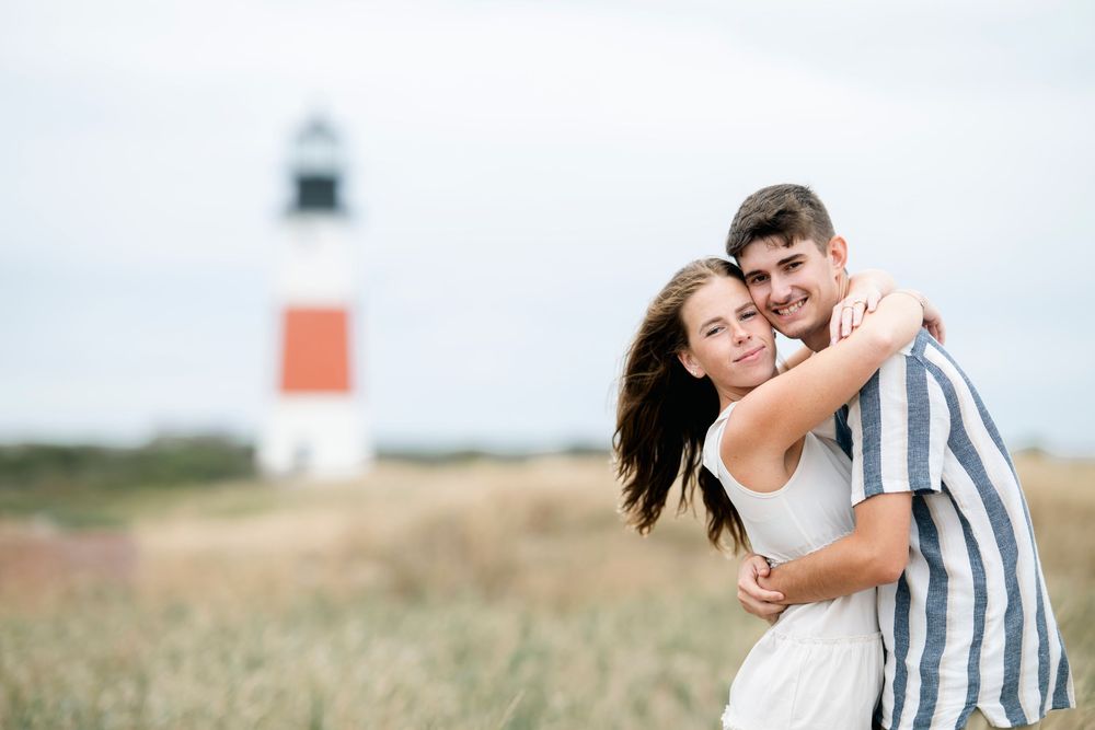 A couple embraces and laughs together in a sunny field during a romantic outdoor photoshoot.