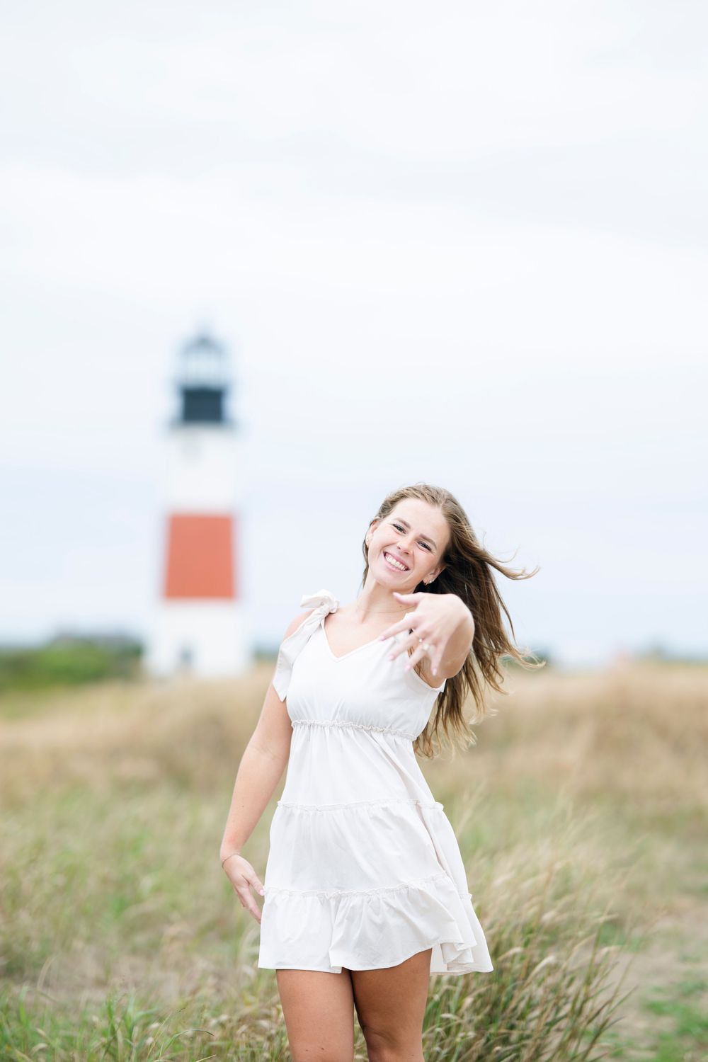 A white sundress flows in the breeze near Sankaty Head Lighthouse in Nantucket on a summer day.