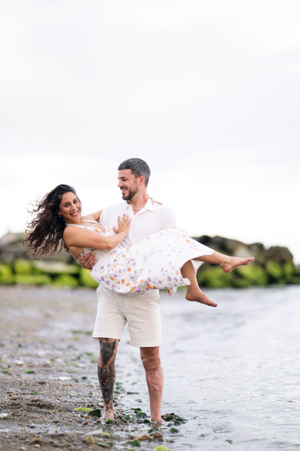 A romantic couple playing and laughing together at the beach shore as waves splash around their feet.