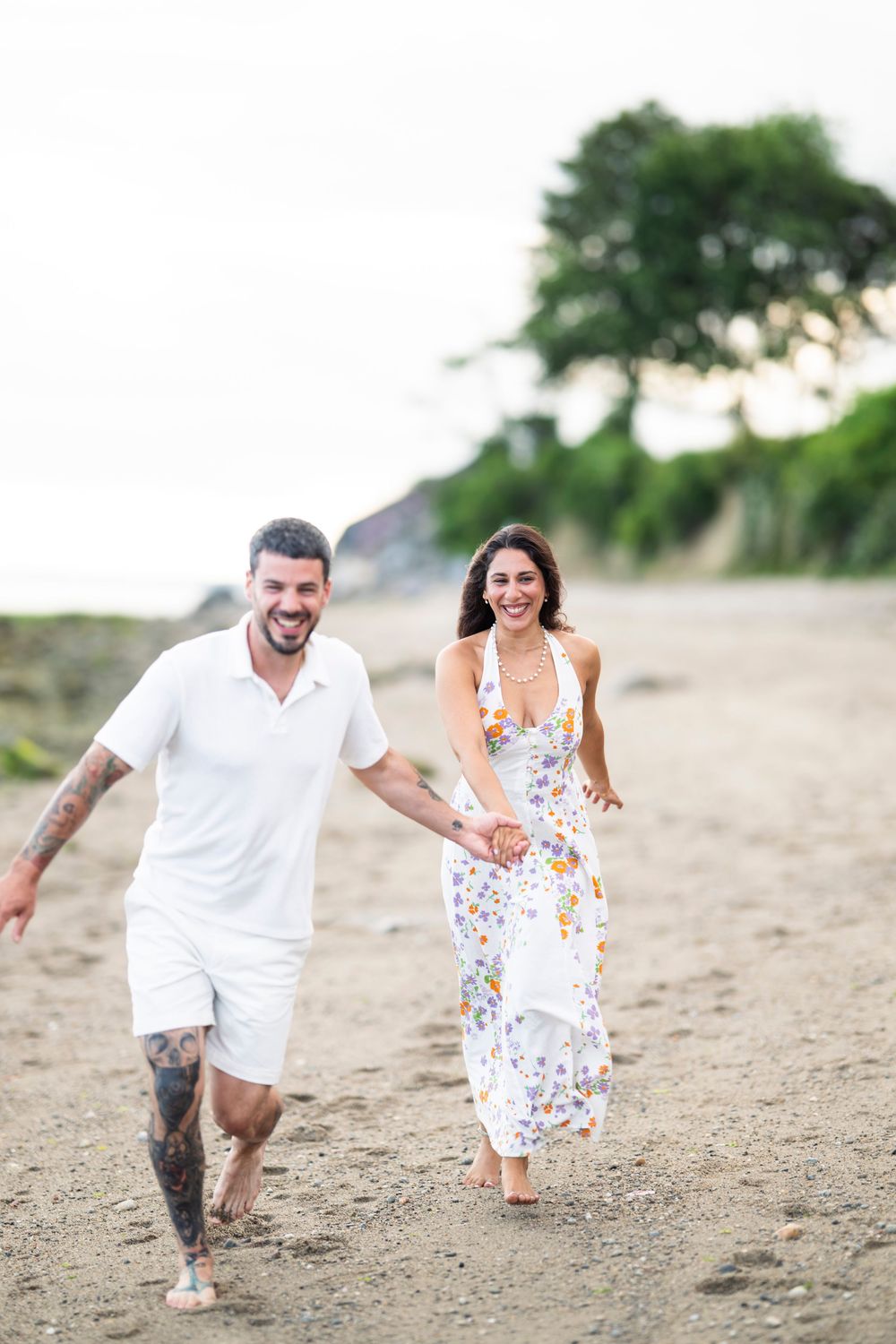 A couple runs playfully together on a sandy beach path during a romantic photoshoot session.