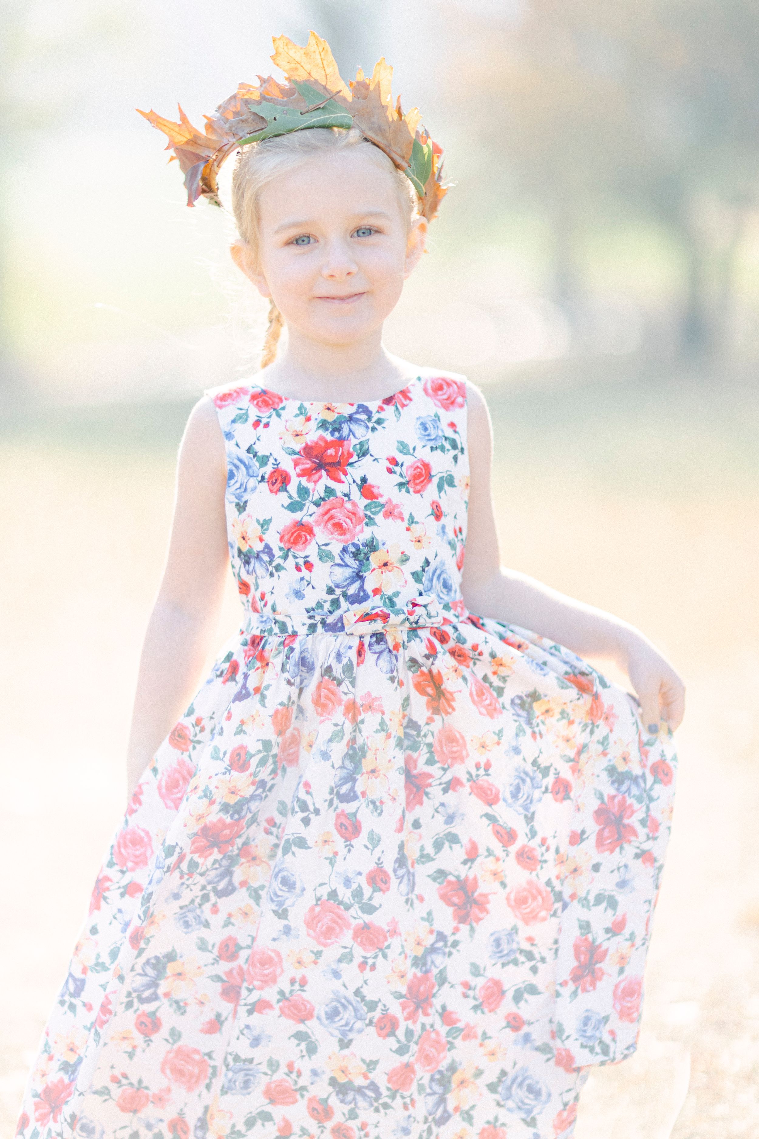 A whimsical portrait featuring a floral dress and autumn leaf crown in soft light.