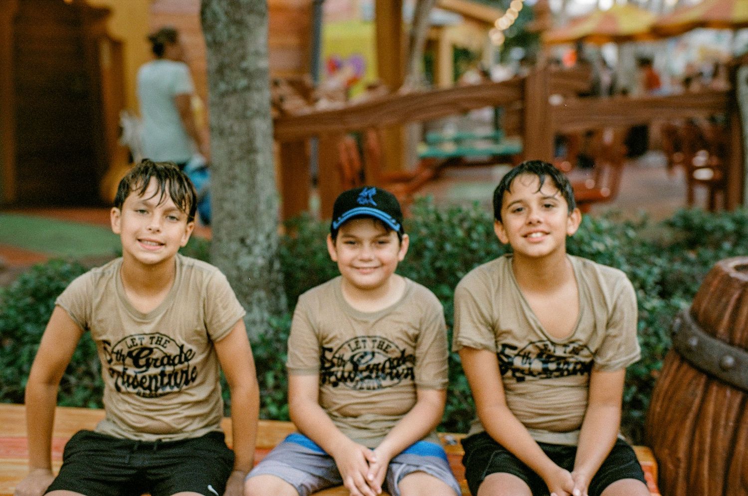 Three people wearing matching t-shirts sit together on a wooden bench.