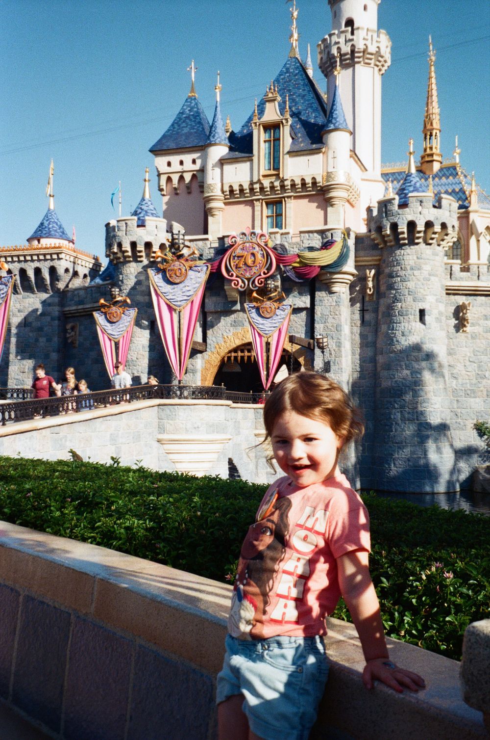 Young girl smiling in front of Sleeping Beauty Castle at Disneyland on a sunny day.