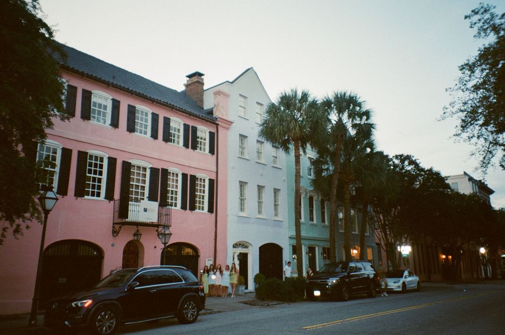Historic Rainbow Row buildings with colorful facades line a Charleston street at dusk with vintage lampposts glowing.