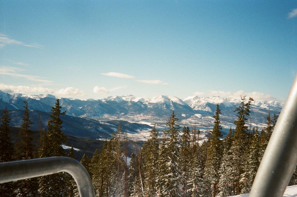 Snow-covered mountain peaks with evergreen trees in foreground viewed from a ski lift in a winter alpine landscape.
