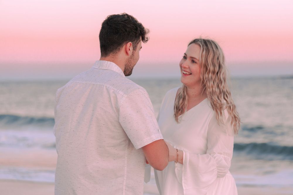 A romantic sunset beach scene with a couple in white outfits by the ocean. Maternity shoot.