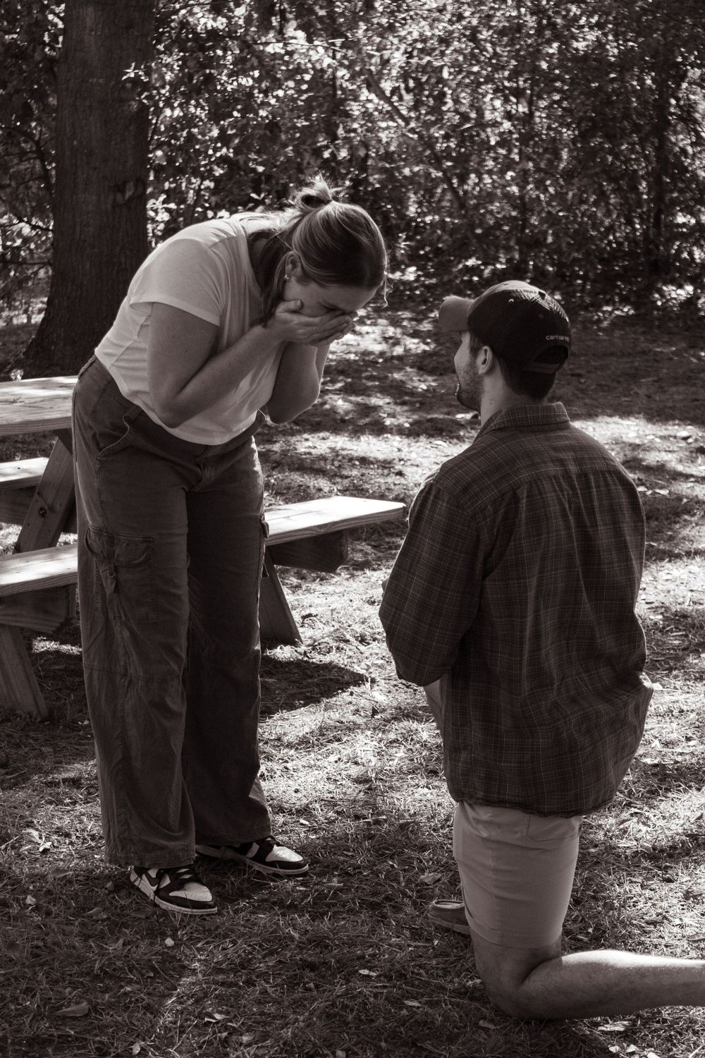 Two people sharing a tender moment in a sunlit outdoor setting with trees in the background.