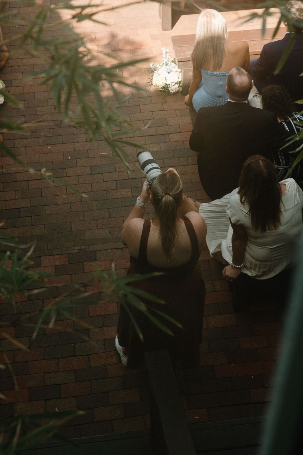 Photographer with professional camera captures a moment at dusk against a brick wall with hanging lantern.
