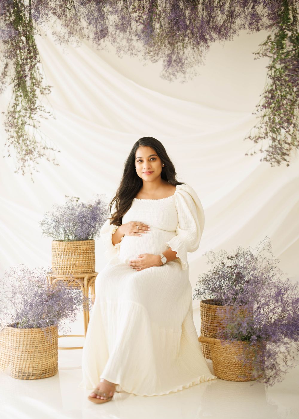 Dreamy maternity photo with lavender decor and woven baskets against a white backdrop.