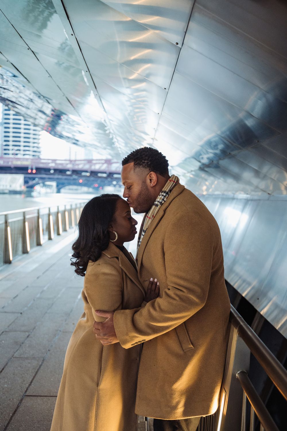 Couple in matching tan coats sharing intimate moment in modern tunnel.