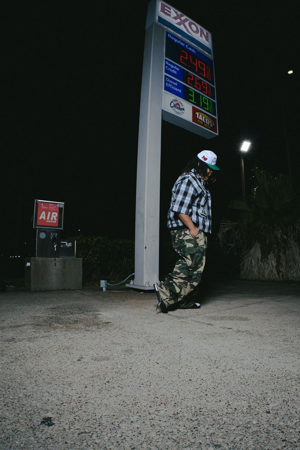 Skateboarder performing trick sequence at night near gas station sign.