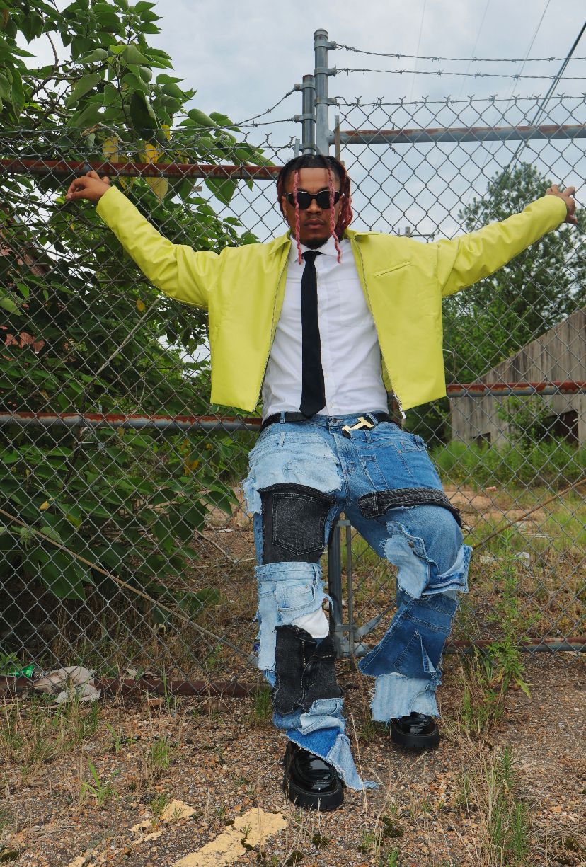 Fashion pose by chain link fence wearing yellow jacket and distressed jeans in outdoor setting.