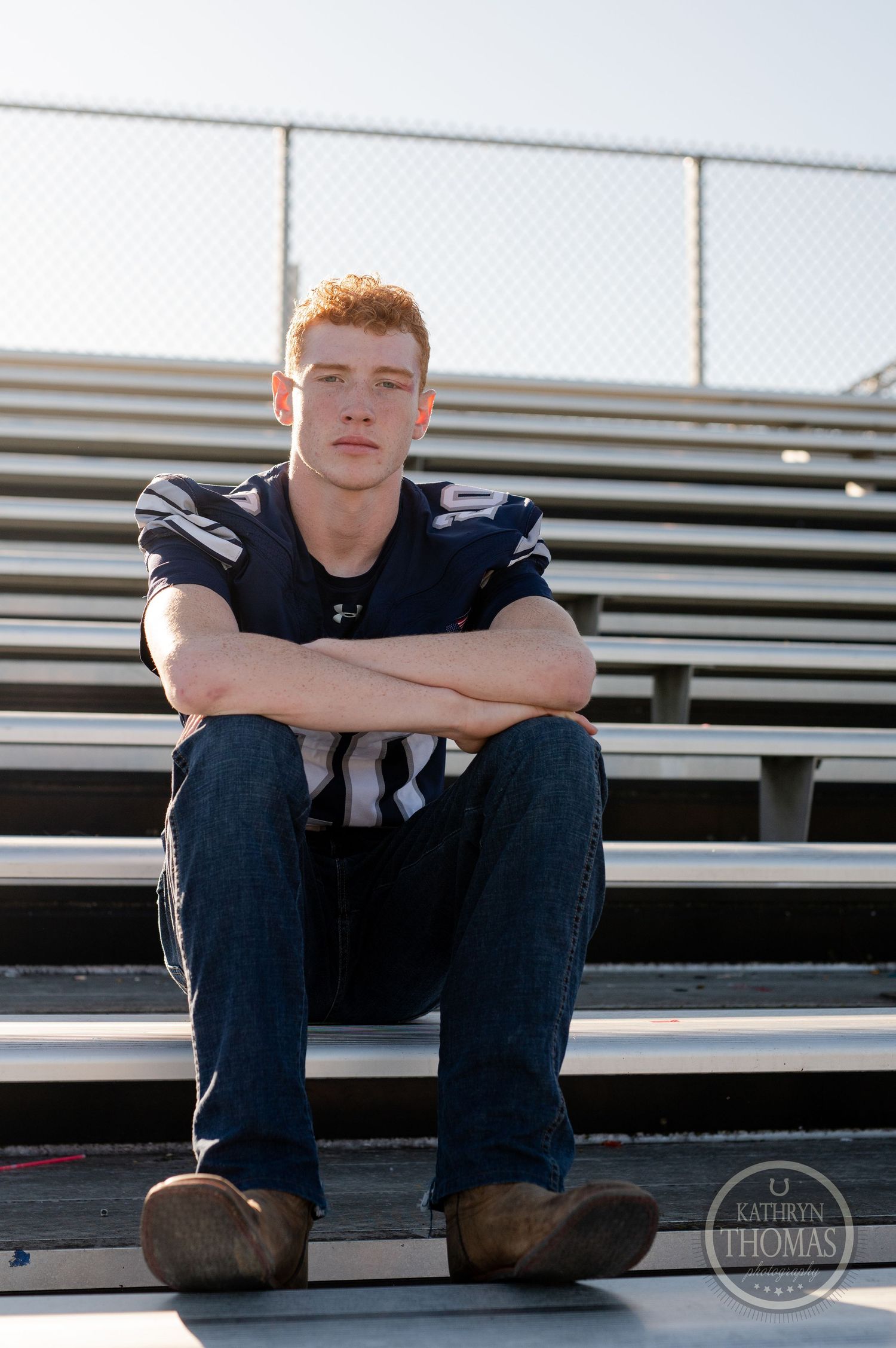 A football player sits on stadium bleachers wearing a navy uniform.