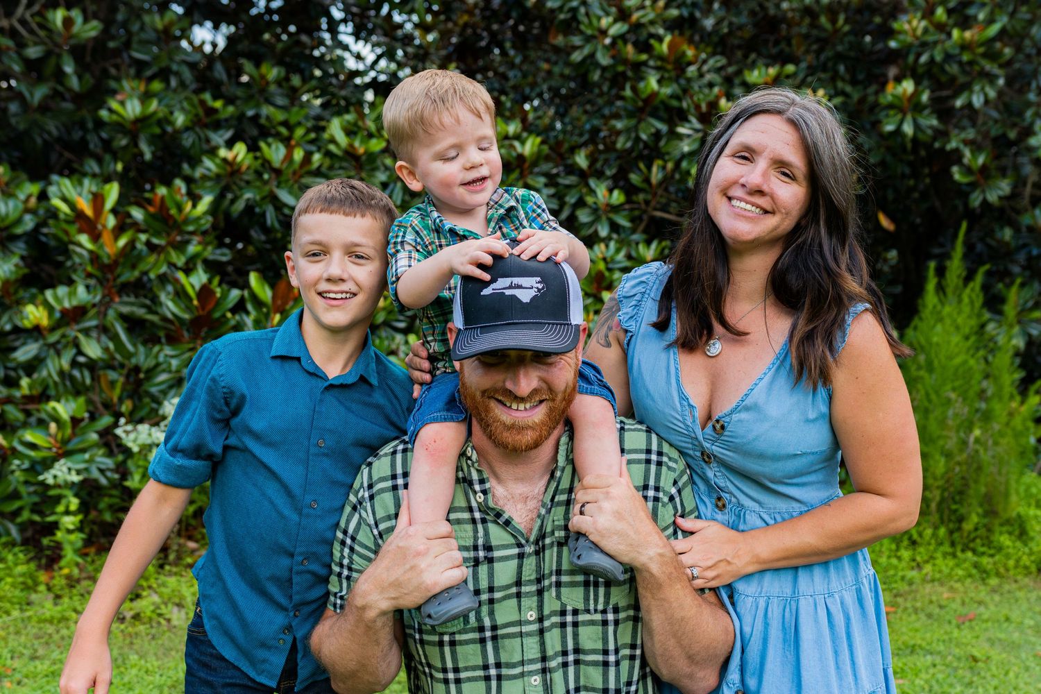 A family of four poses together outdoors during fall with yellow autumn foliage in the background.