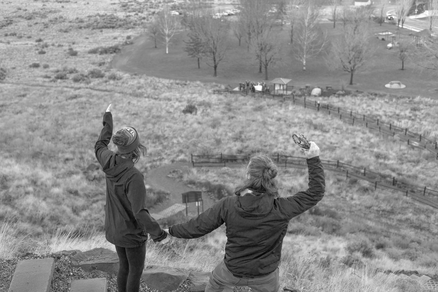 Two bundled figures celebrate joyfully on a hillside overlooking a winter landscape below.