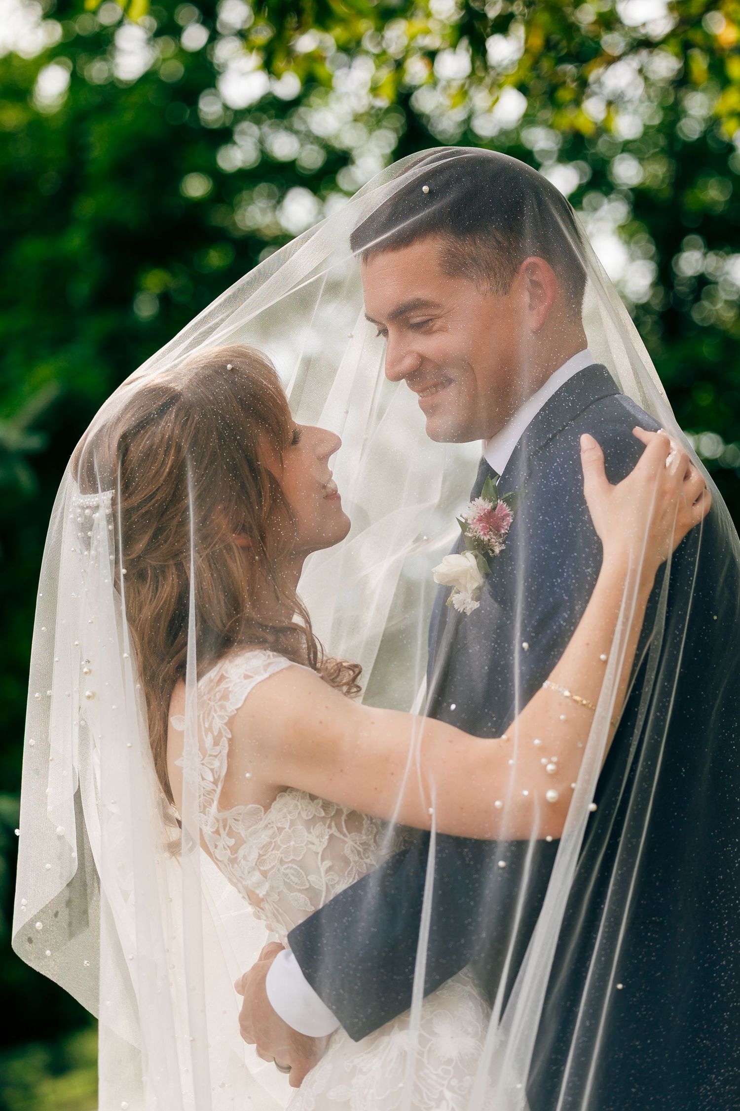 Bride and groom sharing a romantic kiss outdoors, with wedding veil flowing in the breeze on a sunny day.