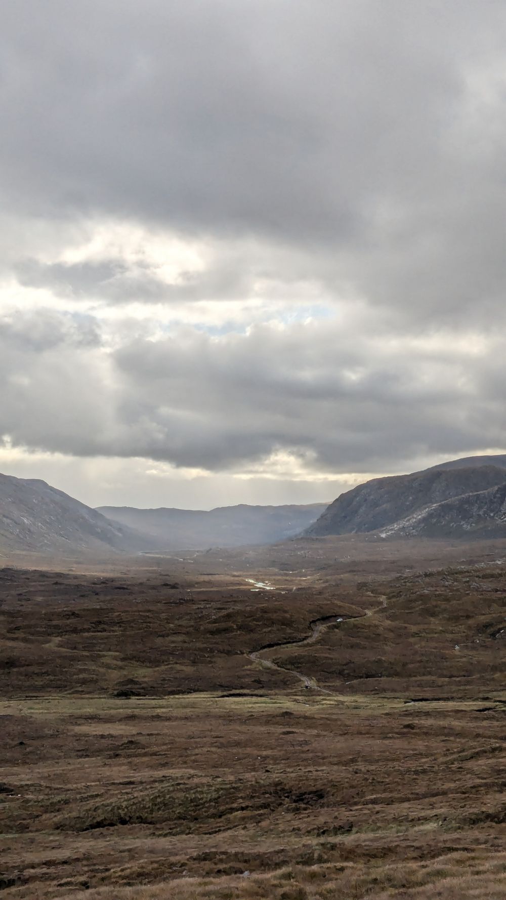 Dramatic cloudy sky over a rugged scottish mountain valley with a winding path through barren moorland landscape.