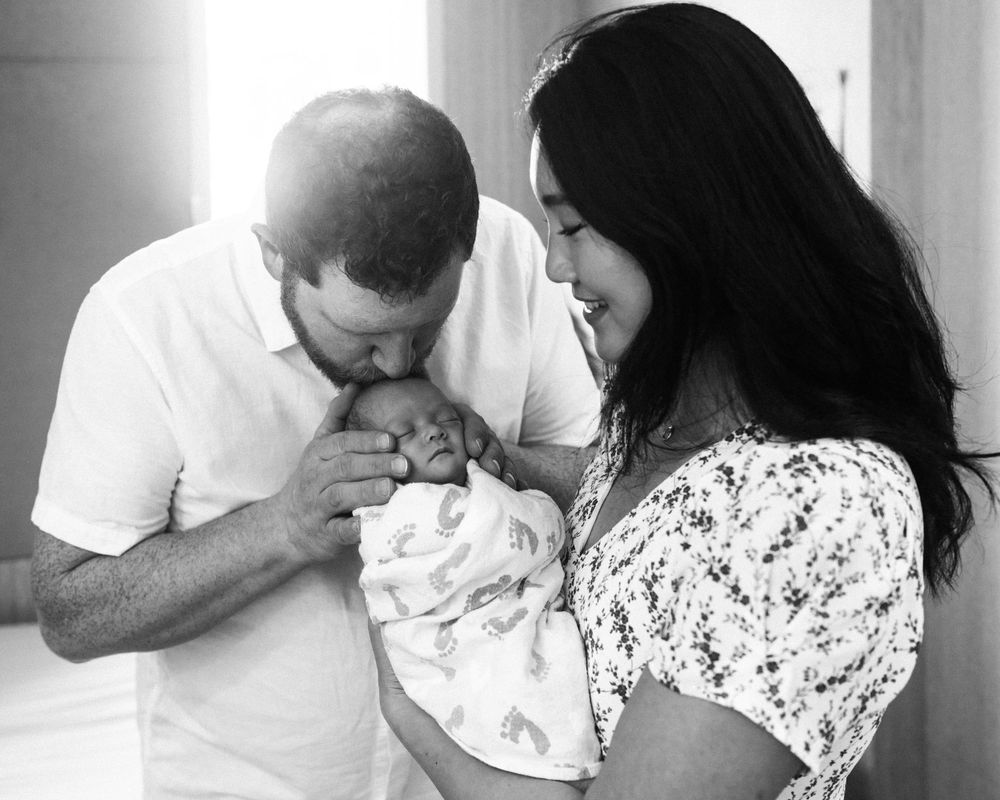 Intimate family moment with newborn baby wrapped in a swaddle blanket.