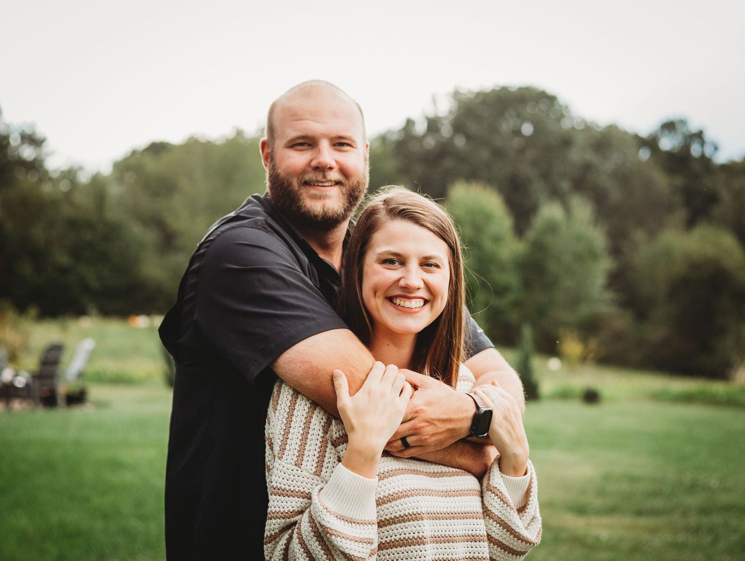 A couple embraces while standing in a grassy field on a sunny day.
