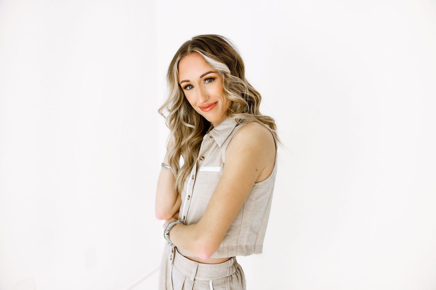 Professional fashion portrait of a person in a light colored sleeveless top against a white background.