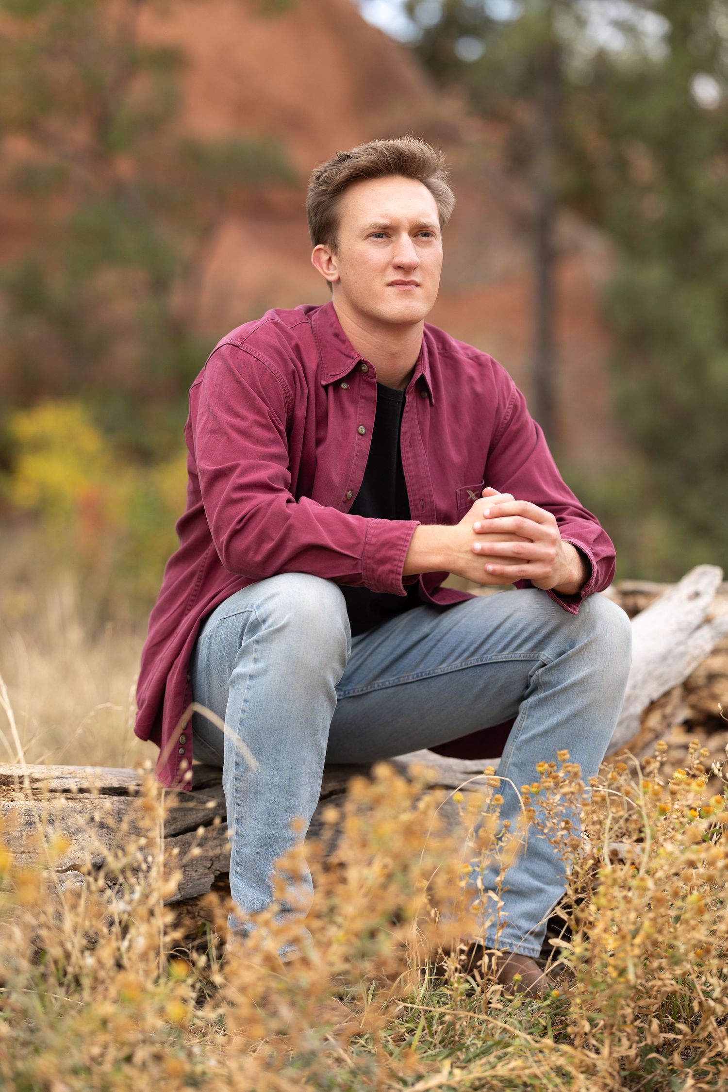 Person in burgundy shirt crouching on natural terrain with reddish rocks behind.