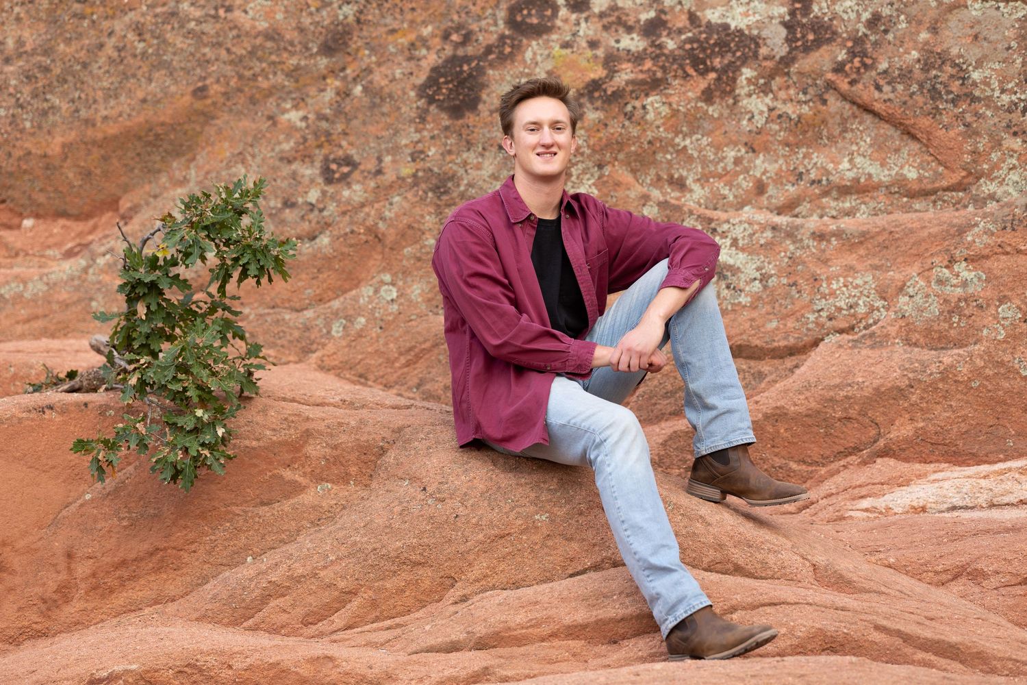 Person in casual attire sitting on red rock formation with desert vegetation.