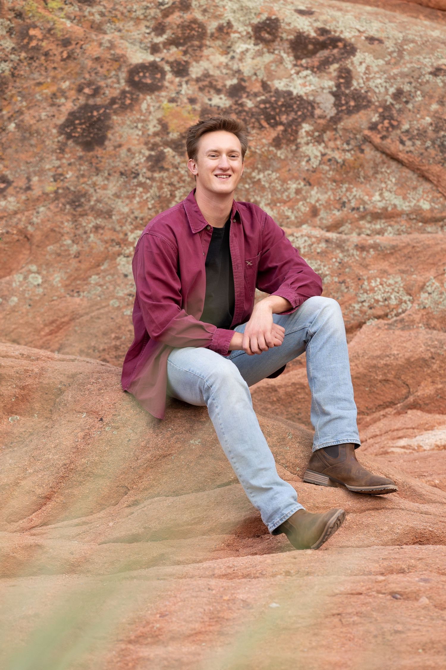 Person sitting on red rock formation wearing burgundy shirt and light jeans.