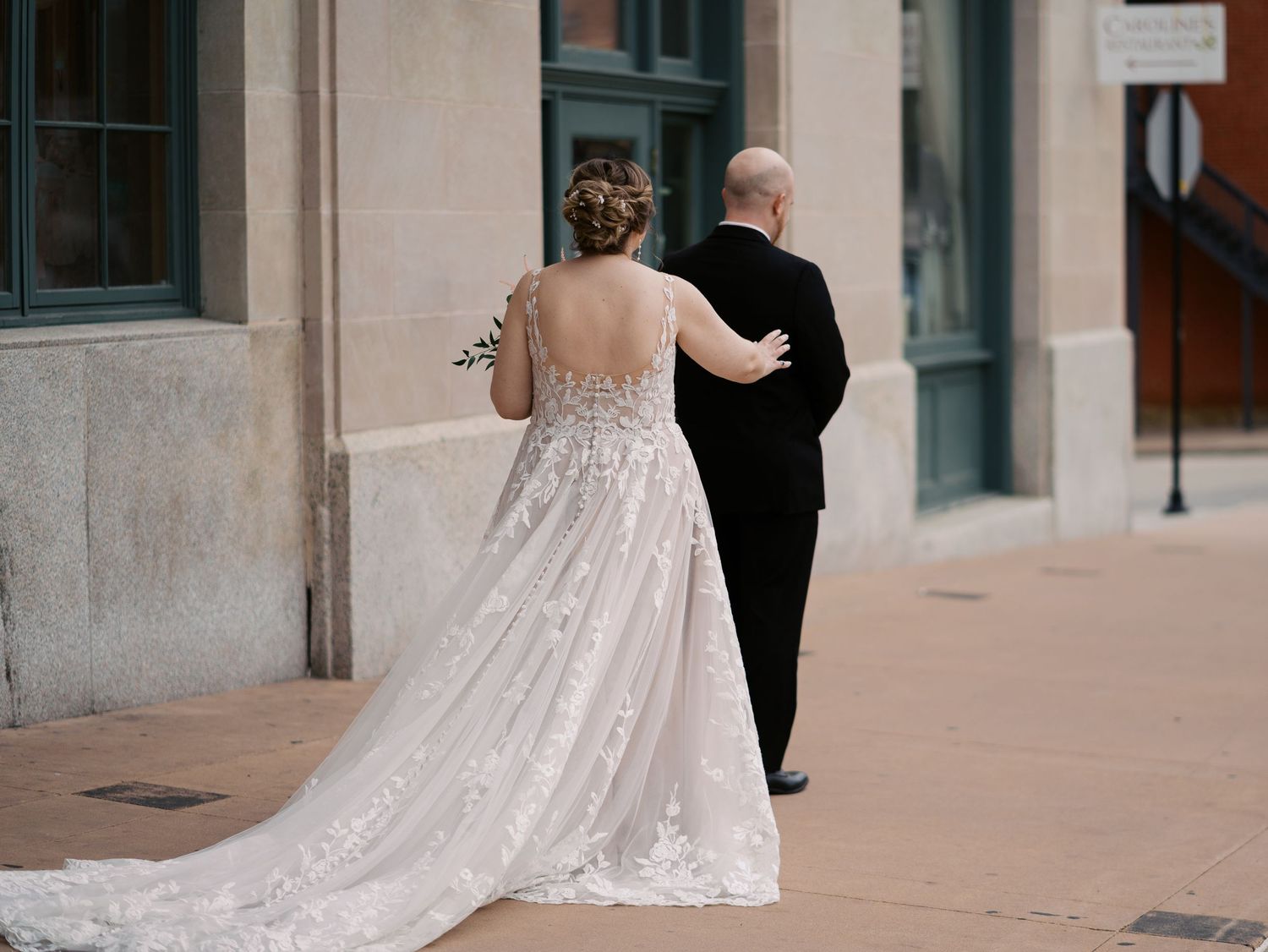 Couple walking together on a sidewalk, with the bride wearing a sparkly white wedding gown and the groom in a black suit.