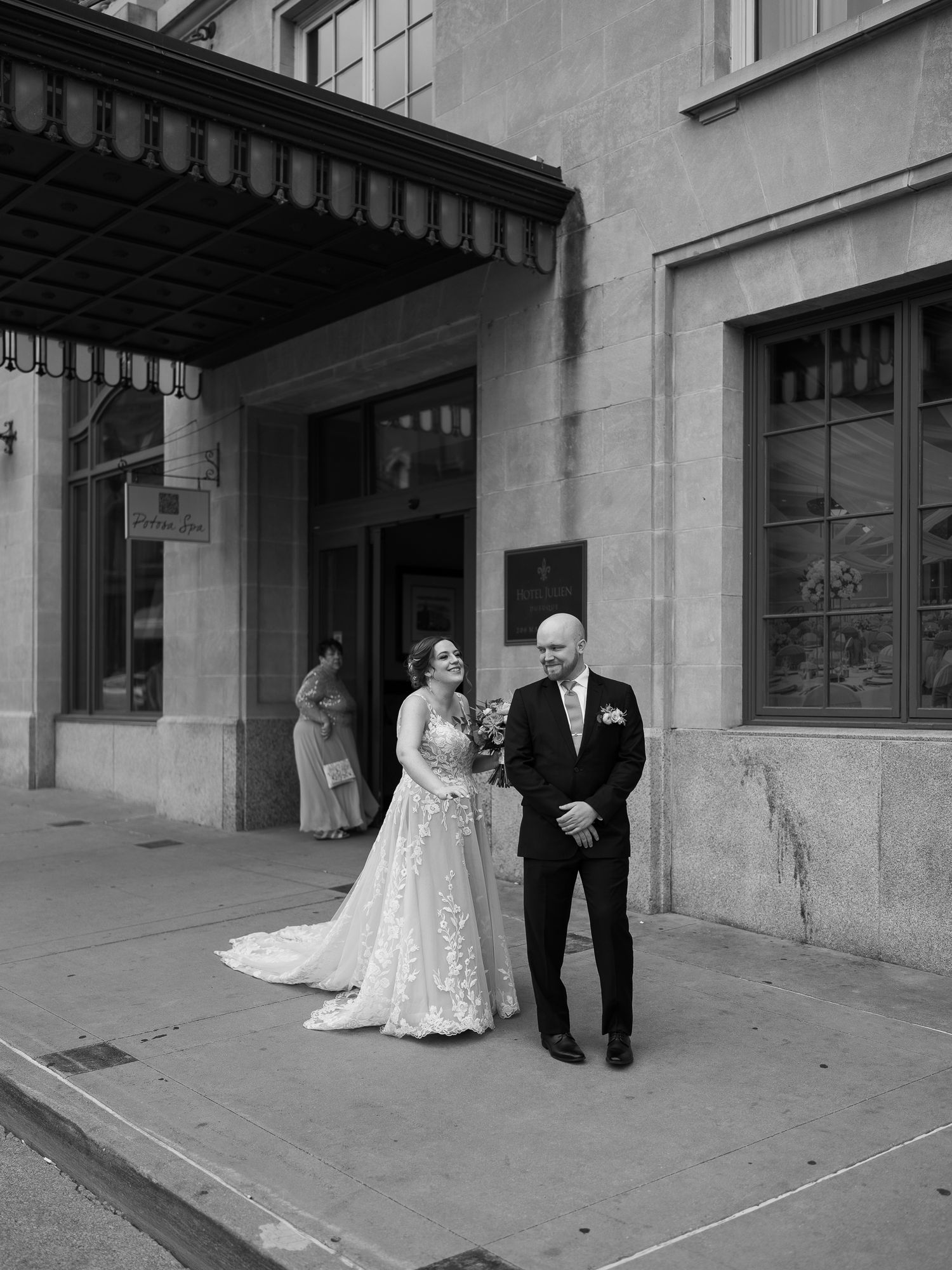 A bride in a lace wedding gown stands under an entrance canopy with an escort before her wedding ceremony.