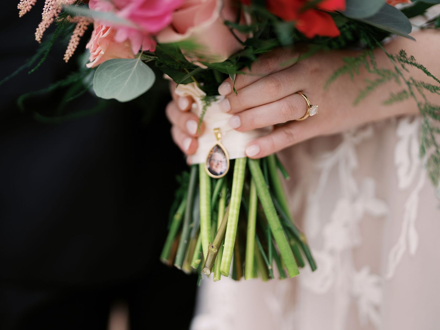 Hands holding a wedding bouquet of pink and red flowers with green stems tied together.