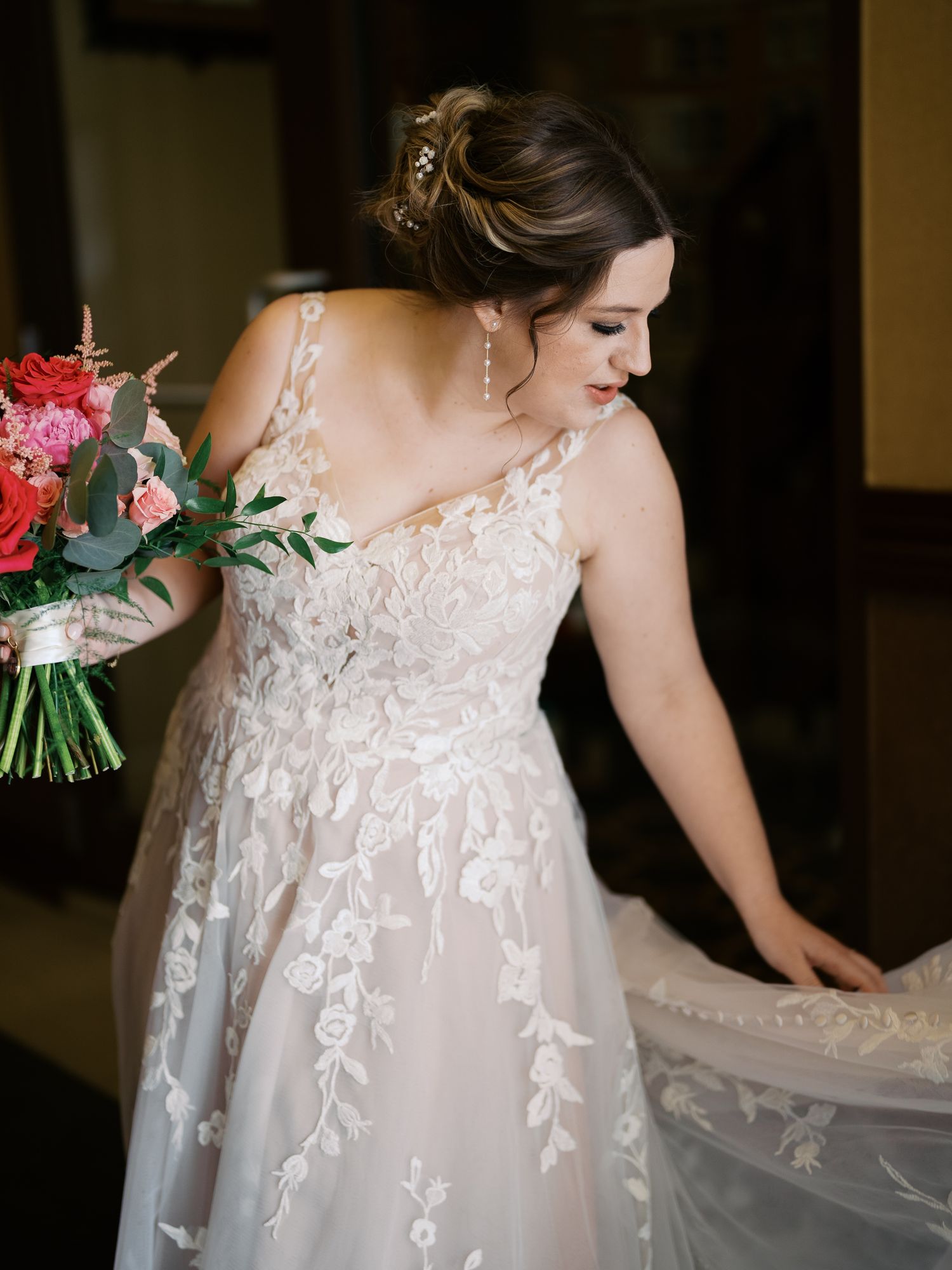 Elegant lace wedding gown with floral appliques and a flowing train shown with red and green bridal bouquet.