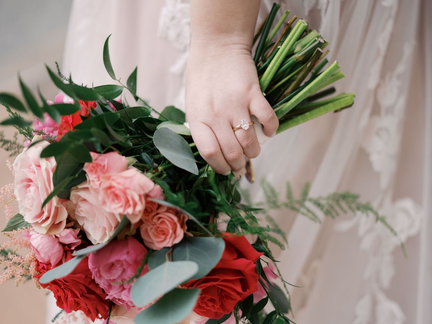 A lush bouquet of pink and red roses with eucalyptus greenery held by a hand wearing an engagement ring.
