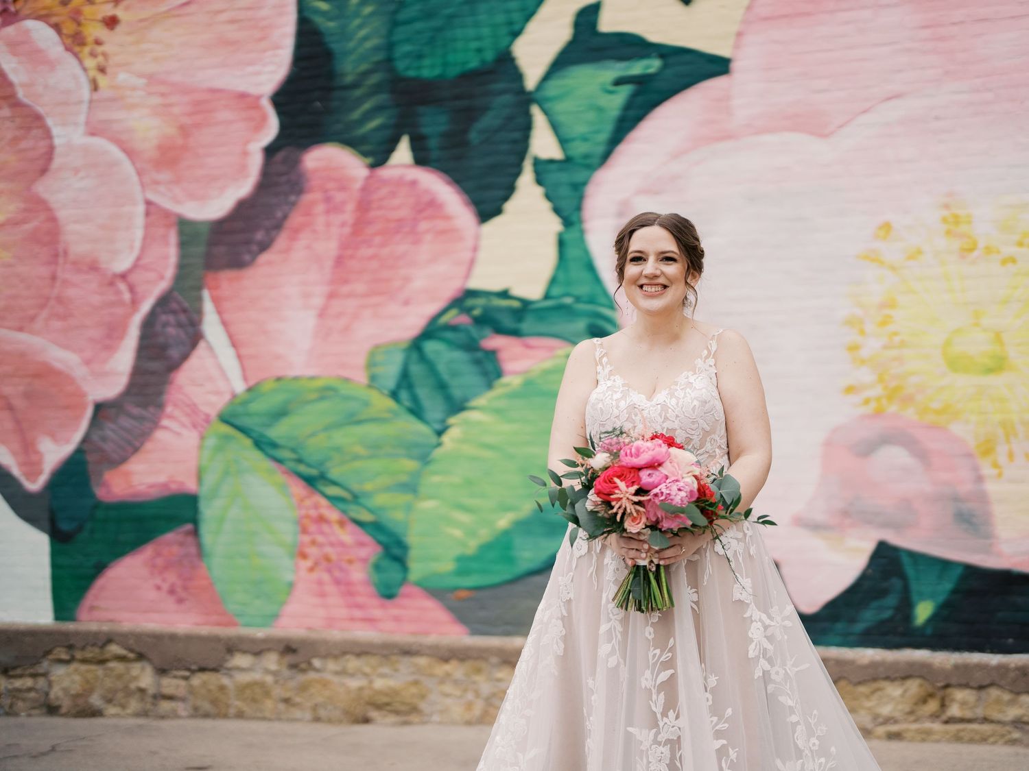 A joyous wedding moment against a floral mural background featuring soft pink blooms and green foliage.