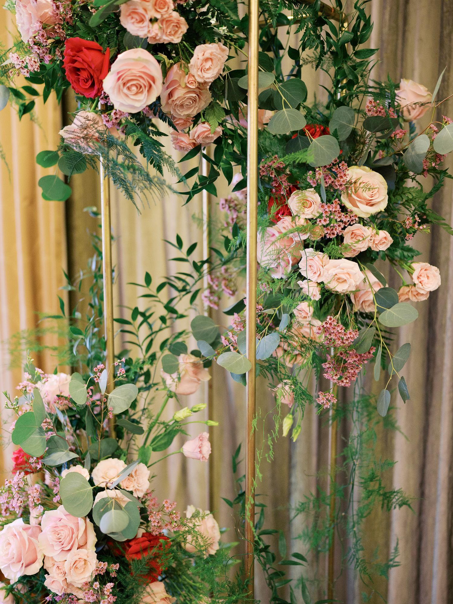 Elegant floral arrangement with pink and peach roses cascading down gold poles with eucalyptus and greenery.