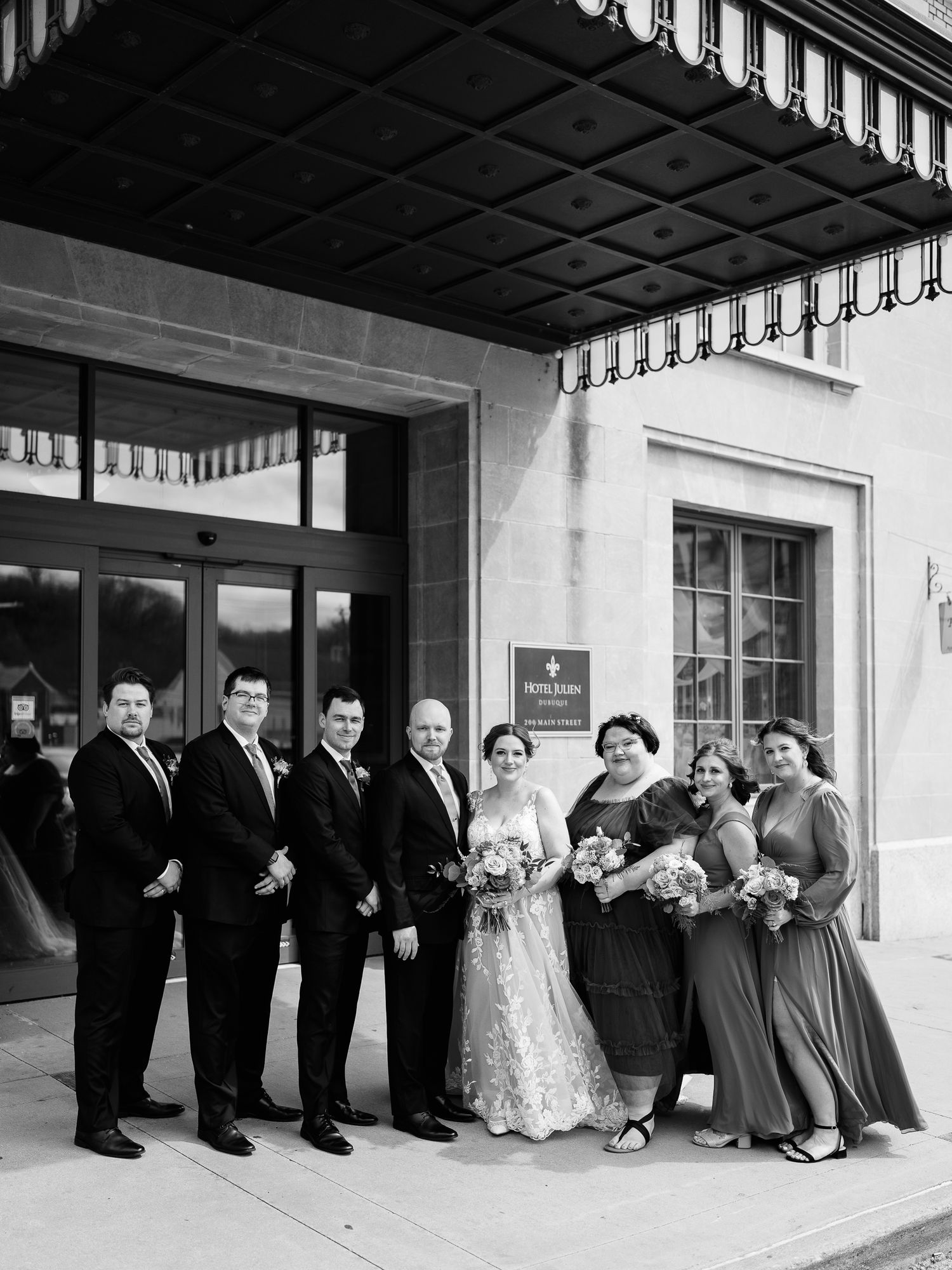 Vintage black and white wedding party photograph showing formal group outside building entrance in classic 1950s style.