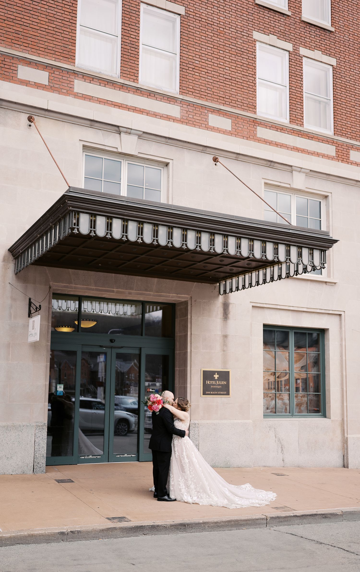 Wedding couple embracing under a classic brick building entrance with black striped awning.
