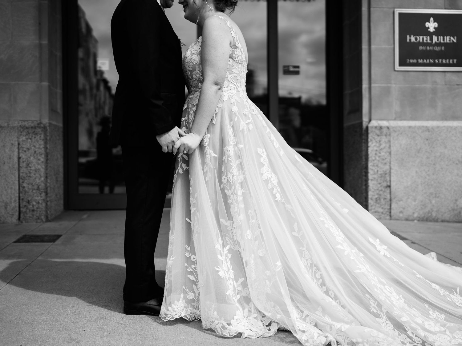An elegant black and white photo showing the intricate lace details of a wedding gown with flowing train.