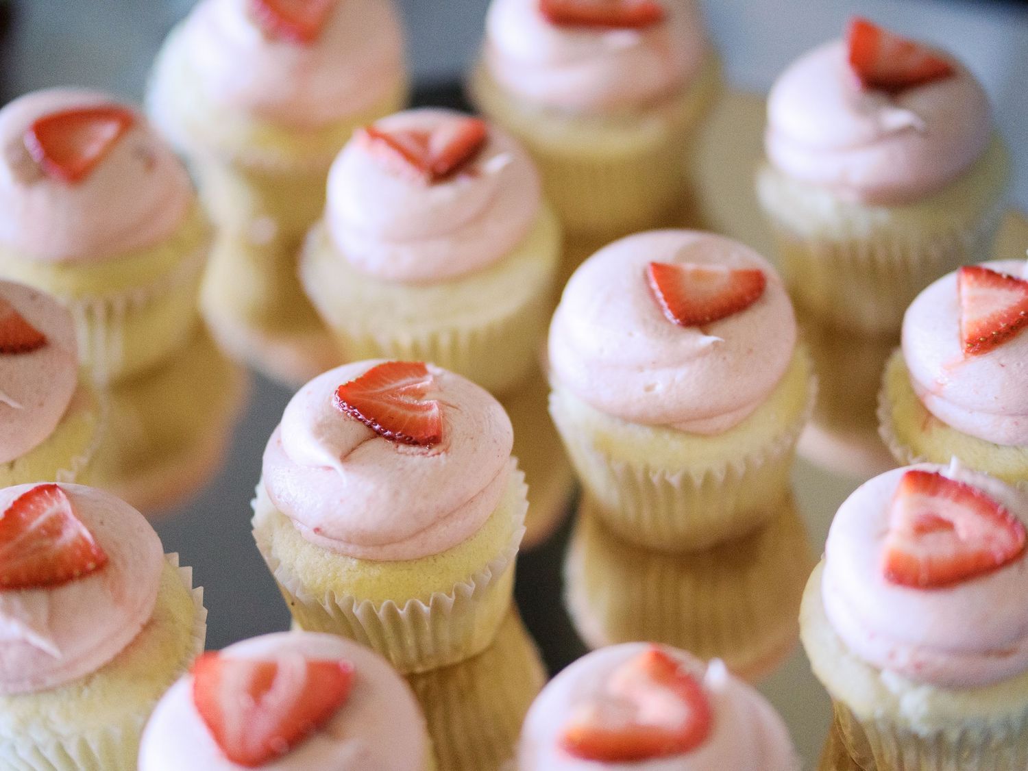 Mini vanilla cupcakes topped with pink frosting and fresh sliced strawberries arranged in neat rows.