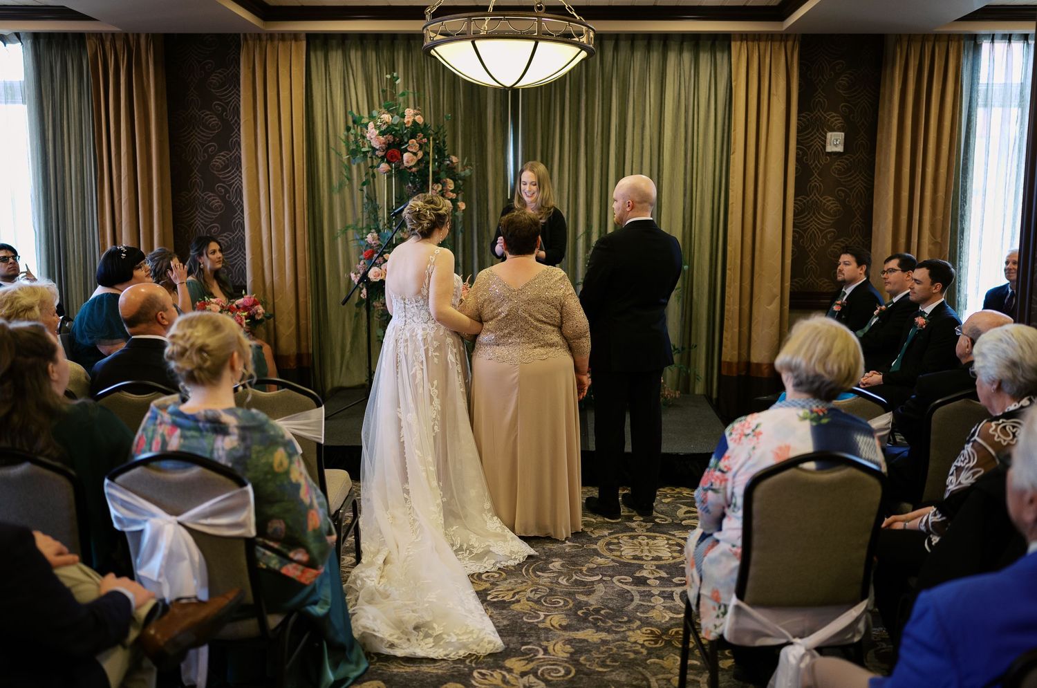 Wedding ceremony in an elegant hotel room with green drapes and traditional seating arrangement.