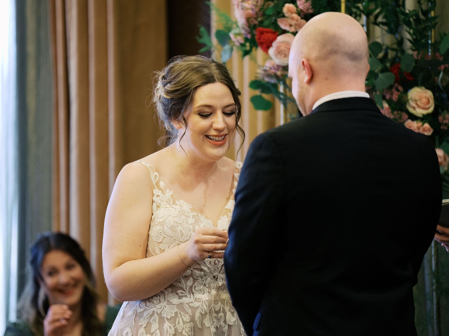 Wedding couple exchanges vows in front of floral arch during intimate indoor ceremony.