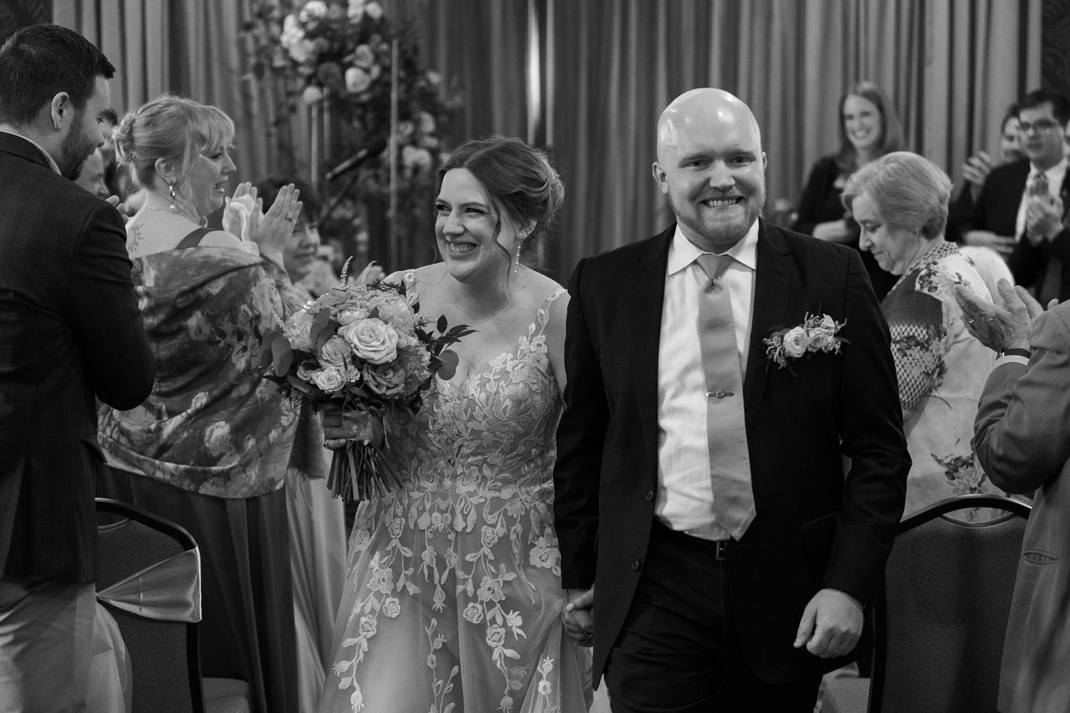 A couple walk together at a wedding reception with decorative curtains and floral arrangements.