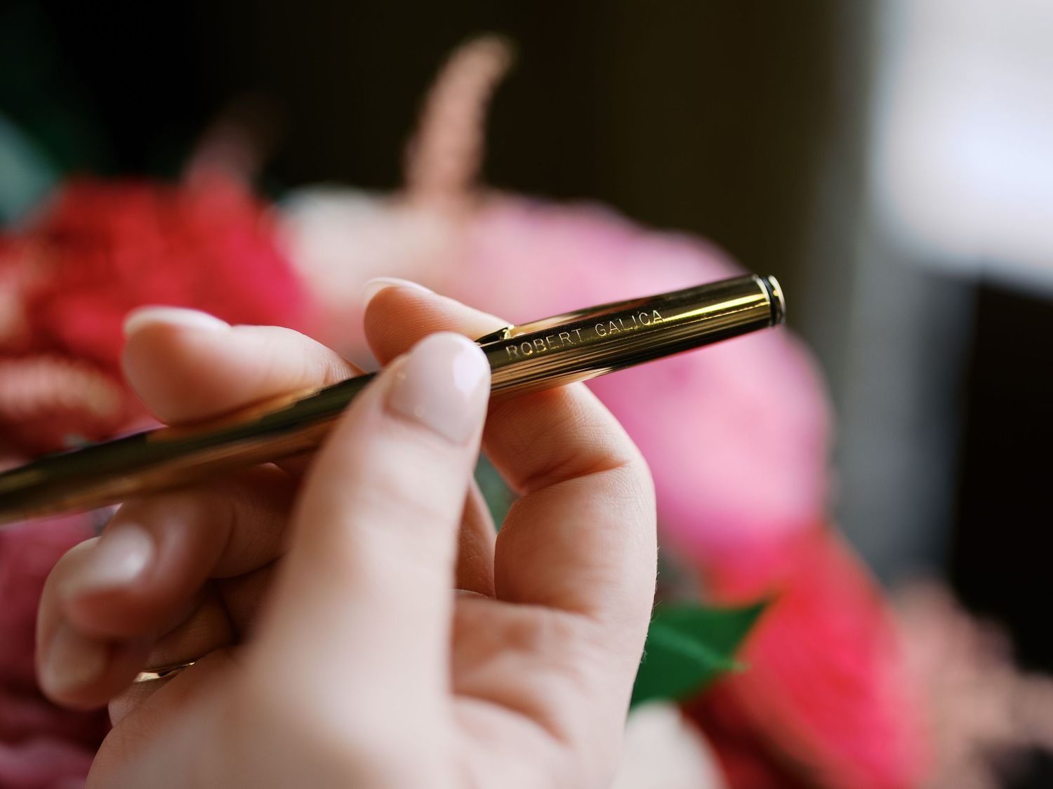 Close-up view of hands holding a golden mechanical pen against a blurred floral background.