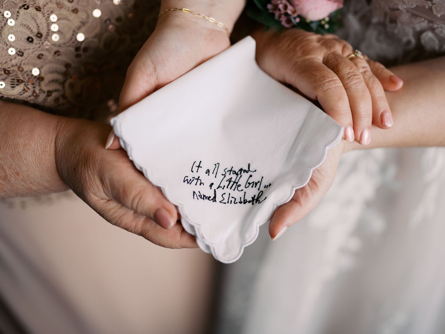 Hands hold a white handkerchief with embroidered text in an elegant wedding setting.