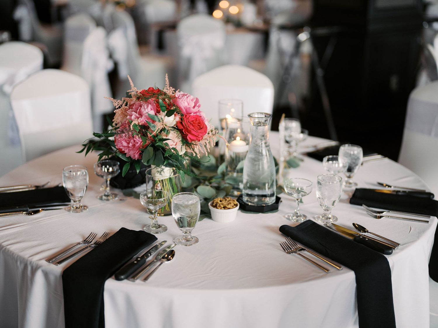 Elegant wedding table setting with pink floral centerpiece, white linens, and black napkins at formal reception.