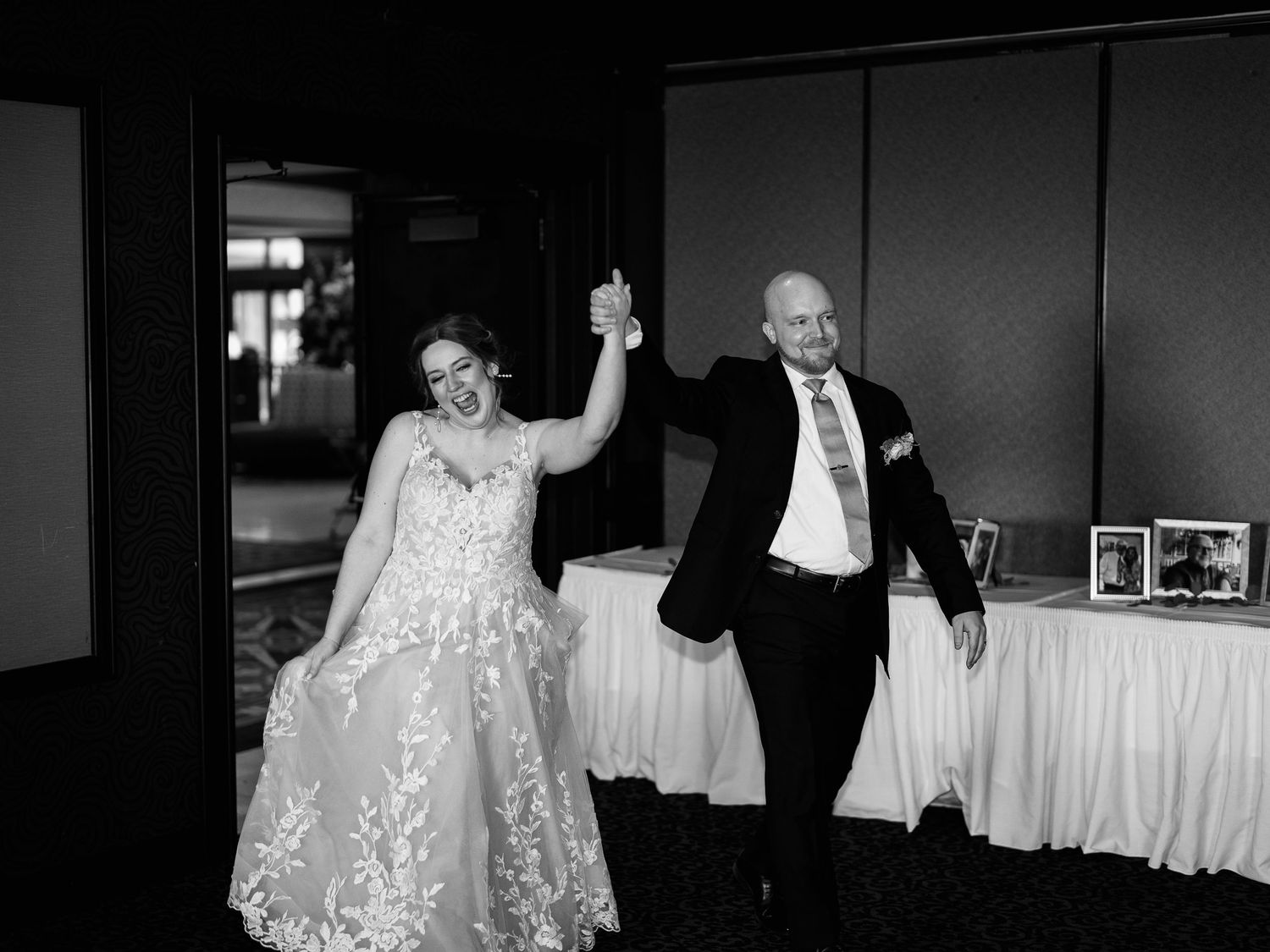 A joyful couple celebrates at their wedding reception, with raised arms and laughter in a black and white photo.