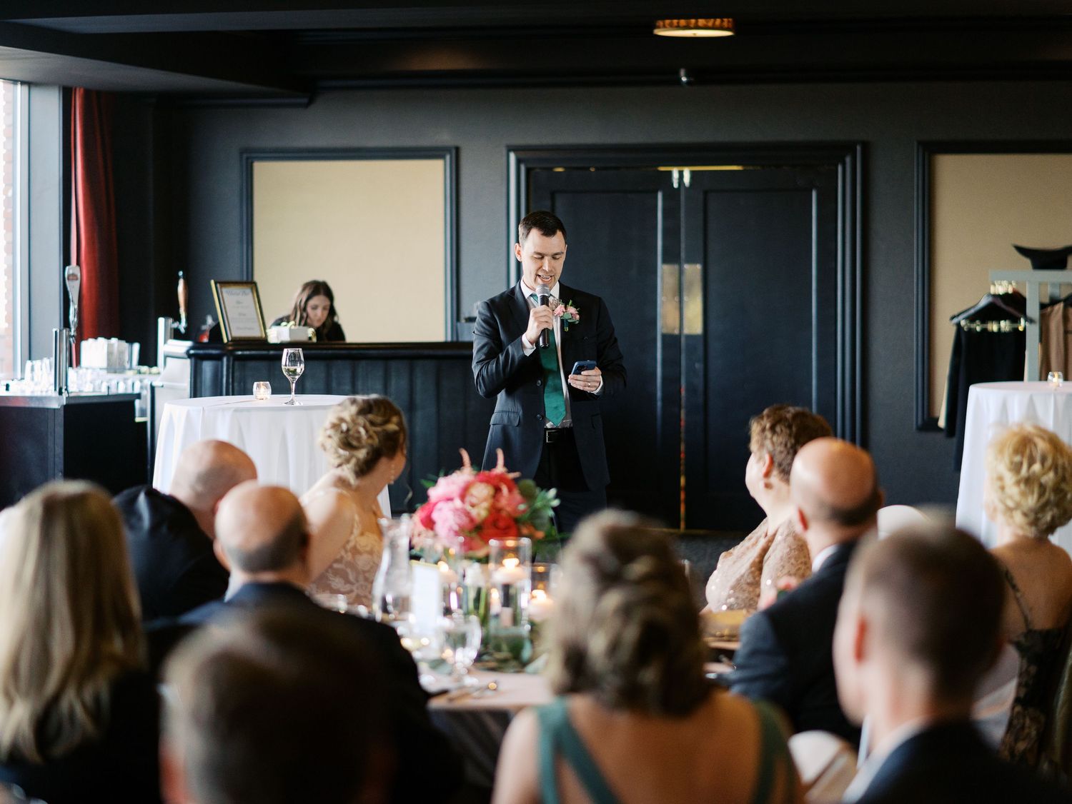 A speaker stands at the front of an elegant dining room filled with guests during an event.